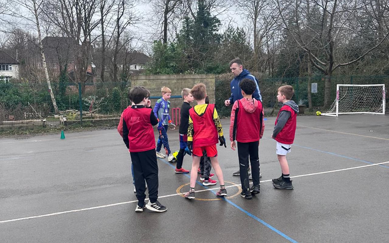 A coach instructing a group of children during an outdoor PE lesson